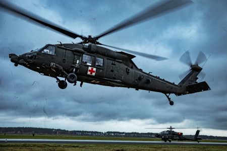 Soldiers assigned to Charlie Company, 2nd Battalion, 501st Aviation Regiment, Combat Aviation Brigade, 1st Armored Division, operationally controlled by the 1st Infantry Division, fly a Blackhawk helicopter during medical evacuation hoist training as an Apache Longbow drives across the taxiway at the 33rd Air Base in Powidz, Poland, Nov. 16, 2022. The soldiers are working alongside NATO allies and regional security partners to provide combat-credible forces to V Corps, America&#39;s forward deployed corps in Europe.