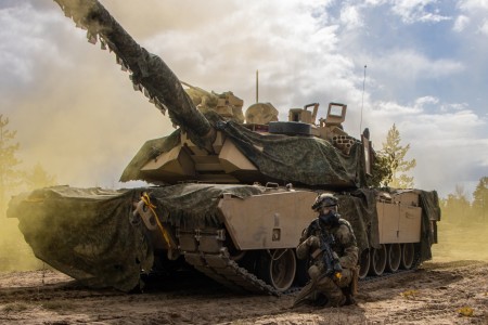 A Soldier kneels in front of an M1A2 SEPV3 Abrams Main Battle Tank, both assigned to 1st Battalion, 8th Cavalry Regiment, during a force-on-force simulated fire training during Arrow 23 in Niinisalo Training Area, Finland, May 5, 2023.